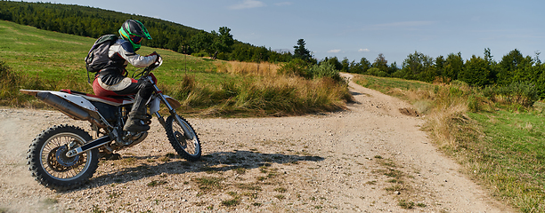 Image showing A professional motocross rider exhilaratingly riding a treacherous off-road forest trail on their motorcycle.