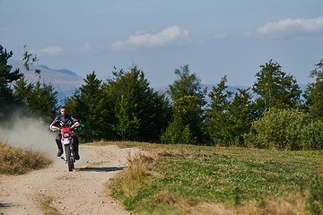 Image showing A professional motocross rider exhilaratingly riding a treacherous off-road forest trail on their motorcycle.