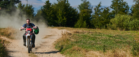 Image showing A professional motocross rider exhilaratingly riding a treacherous off-road forest trail on their motorcycle.