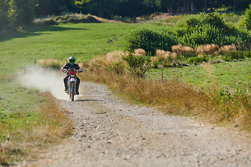 Image showing A professional motocross rider exhilaratingly riding a treacherous off-road forest trail on their motorcycle.