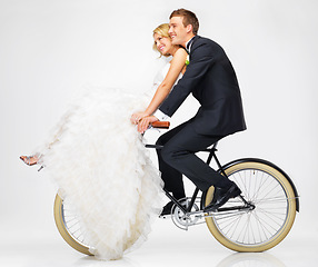 Image showing Happy, wedding and couple on a bicycle against a white background, after getting married together. Love, young bride and groom in dress and suit, cycling on a bike in marriage happiness or bliss