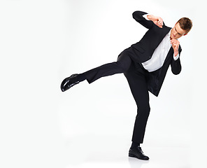 Image showing Business man doing a karate kick to the side while standing in a studio with copy space. Man in suit working on his fitness with martial arts training. Professional spy agent practicing to fight.