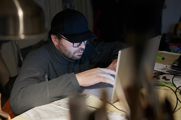 Image showing A close-up shot of a man using a laptop in a dimly lit room, engrossed in his digital work during the late hours of the night