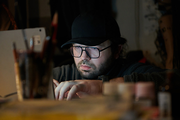 Image showing A close-up shot of a man using a laptop in a dimly lit room, engrossed in his digital work during the late hours of the night