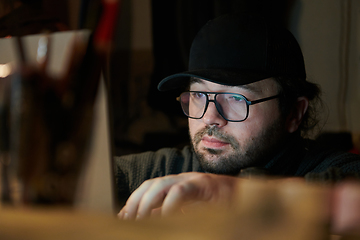 Image showing A close-up shot of a man using a laptop in a dimly lit room, engrossed in his digital work during the late hours of the night