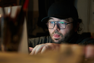 Image showing A close-up shot of a man using a laptop in a dimly lit room, engrossed in his digital work during the late hours of the night