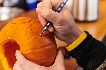 Image showing A modern blonde woman in military uniform is carving spooky pumpkins with a knife for Halloween night