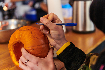 Image showing A modern blonde woman in military uniform is carving spooky pumpkins with a knife for Halloween night