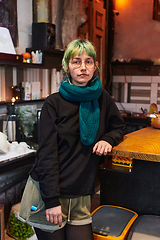 Image showing A modern and intriguing girl with striking blue hair enjoys a night out in a cafe transformed into a passionate Halloween-style setting, exuding a captivating and witchy ambiance