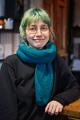 Image showing A modern and intriguing girl with striking blue hair enjoys a night out in a cafe transformed into a passionate Halloween-style setting, exuding a captivating and witchy ambiance