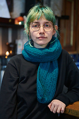 Image showing A modern and intriguing girl with striking blue hair enjoys a night out in a cafe transformed into a passionate Halloween-style setting, exuding a captivating and witchy ambiance