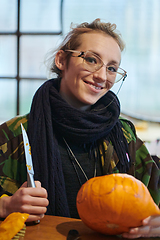 Image showing A modern blonde woman in military uniform is carving spooky pumpkins with a knife for Halloween night