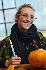 Image showing A modern blonde woman in military uniform is carving spooky pumpkins with a knife for Halloween night