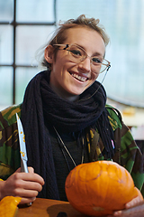 Image showing A modern blonde woman in military uniform is carving spooky pumpkins with a knife for Halloween night