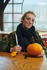 Image showing A modern blonde woman in military uniform is carving spooky pumpkins with a knife for Halloween night