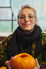 Image showing A modern blonde woman in military uniform is carving spooky pumpkins with a knife for Halloween night