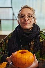 Image showing A modern blonde woman in military uniform is carving spooky pumpkins with a knife for Halloween night