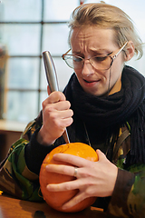 Image showing A modern blonde woman in military uniform is carving spooky pumpkins with a knife for Halloween night