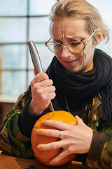 Image showing A modern blonde woman in military uniform is carving spooky pumpkins with a knife for Halloween night