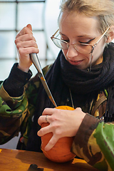 Image showing A modern blonde woman in military uniform is carving spooky pumpkins with a knife for Halloween night