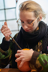 Image showing A modern blonde woman in military uniform is carving spooky pumpkins with a knife for Halloween night