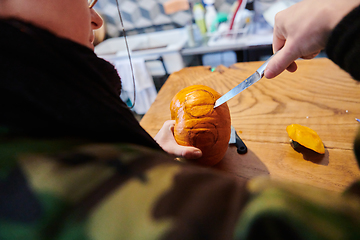 Image showing A modern blonde woman in military uniform is carving spooky pumpkins with a knife for Halloween night