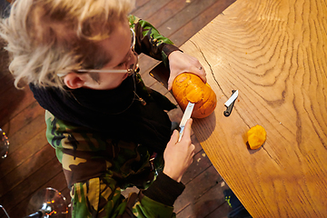 Image showing A modern blonde woman in military uniform is carving spooky pumpkins with a knife for Halloween night