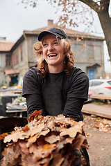 Image showing A stylish, modern young woman takes on the role of a garden caretaker, diligently collecting old, dry leaves and cleaning up the yard in an eco-conscious manner