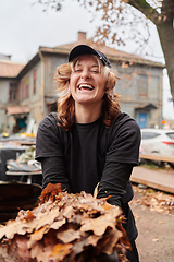 Image showing A stylish, modern young woman takes on the role of a garden caretaker, diligently collecting old, dry leaves and cleaning up the yard in an eco-conscious manner