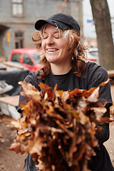 Image showing A stylish, modern young woman takes on the role of a garden caretaker, diligently collecting old, dry leaves and cleaning up the yard in an eco-conscious manner