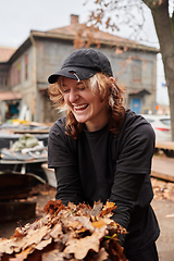 Image showing A stylish, modern young woman takes on the role of a garden caretaker, diligently collecting old, dry leaves and cleaning up the yard in an eco-conscious manner