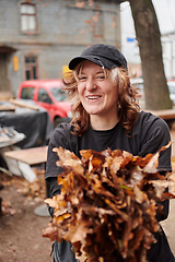 Image showing A stylish, modern young woman takes on the role of a garden caretaker, diligently collecting old, dry leaves and cleaning up the yard in an eco-conscious manner