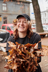 Image showing A stylish, modern young woman takes on the role of a garden caretaker, diligently collecting old, dry leaves and cleaning up the yard in an eco-conscious manner