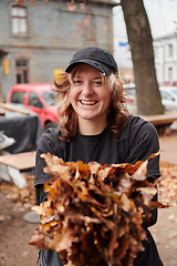 Image showing A stylish, modern young woman takes on the role of a garden caretaker, diligently collecting old, dry leaves and cleaning up the yard in an eco-conscious manner