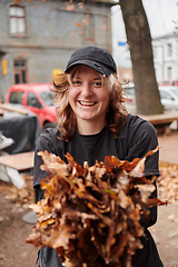 Image showing A stylish, modern young woman takes on the role of a garden caretaker, diligently collecting old, dry leaves and cleaning up the yard in an eco-conscious manner