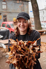 Image showing A stylish, modern young woman takes on the role of a garden caretaker, diligently collecting old, dry leaves and cleaning up the yard in an eco-conscious manner