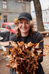 Image showing A stylish, modern young woman takes on the role of a garden caretaker, diligently collecting old, dry leaves and cleaning up the yard in an eco-conscious manner