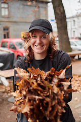 Image showing A stylish, modern young woman takes on the role of a garden caretaker, diligently collecting old, dry leaves and cleaning up the yard in an eco-conscious manner