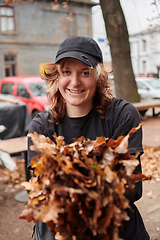 Image showing A stylish, modern young woman takes on the role of a garden caretaker, diligently collecting old, dry leaves and cleaning up the yard in an eco-conscious manner