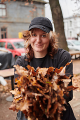 Image showing A stylish, modern young woman takes on the role of a garden caretaker, diligently collecting old, dry leaves and cleaning up the yard in an eco-conscious manner