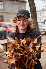 Image showing A stylish, modern young woman takes on the role of a garden caretaker, diligently collecting old, dry leaves and cleaning up the yard in an eco-conscious manner