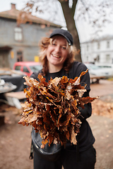 Image showing A stylish, modern young woman takes on the role of a garden caretaker, diligently collecting old, dry leaves and cleaning up the yard in an eco-conscious manner