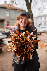 Image showing A stylish, modern young woman takes on the role of a garden caretaker, diligently collecting old, dry leaves and cleaning up the yard in an eco-conscious manner