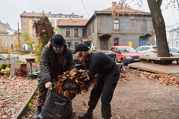 Image showing Father-daughter duo bonding in the garden as they work together to collect fallen leaves and fill up a bag on a crisp autumn day.