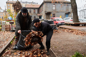 Image showing Father-daughter duo bonding in the garden as they work together to collect fallen leaves and fill up a bag on a crisp autumn day.