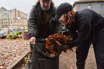 Image showing Father-daughter duo bonding in the garden as they work together to collect fallen leaves and fill up a bag on a crisp autumn day.