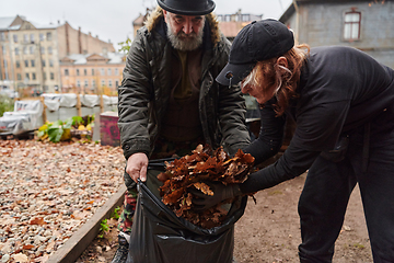 Image showing Father-daughter duo bonding in the garden as they work together to collect fallen leaves and fill up a bag on a crisp autumn day.