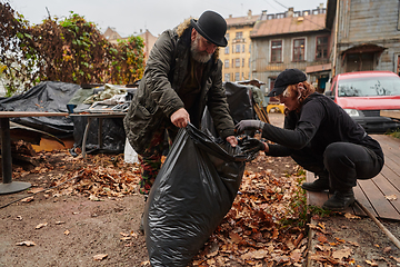 Image showing Father-daughter duo bonding in the garden as they work together to collect fallen leaves and fill up a bag on a crisp autumn day.