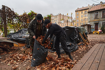 Image showing Father-daughter duo bonding in the garden as they work together to collect fallen leaves and fill up a bag on a crisp autumn day.