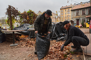 Image showing Father-daughter duo bonding in the garden as they work together to collect fallen leaves and fill up a bag on a crisp autumn day.